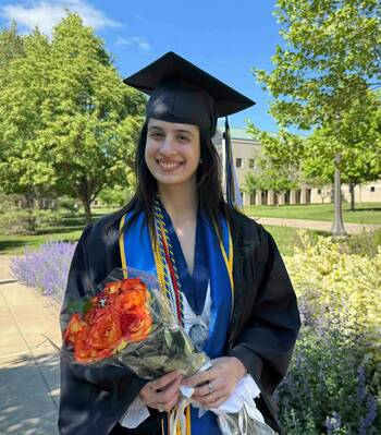 Júlia smiles on graduation day in her cap and gown, holding a bouquet of flowers