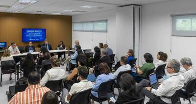 A diverse audience listens attentively to four panelists at a table, visible under a screen displaying "Bridging Worlds: Cultivating Research Partnerships for Climate Hope." The event, hosted by University of Notre Dame São Paulo, takes place in a modern conference room.